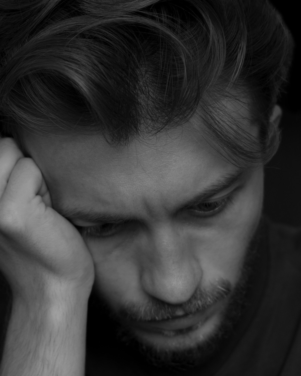 A pensive man resting his head on his hand, looking down in thought